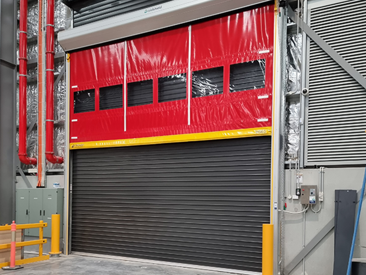 Industrial warehouse interior showing a Movidor HS series high speed rapid roll door in front of a custom insulated sectional door